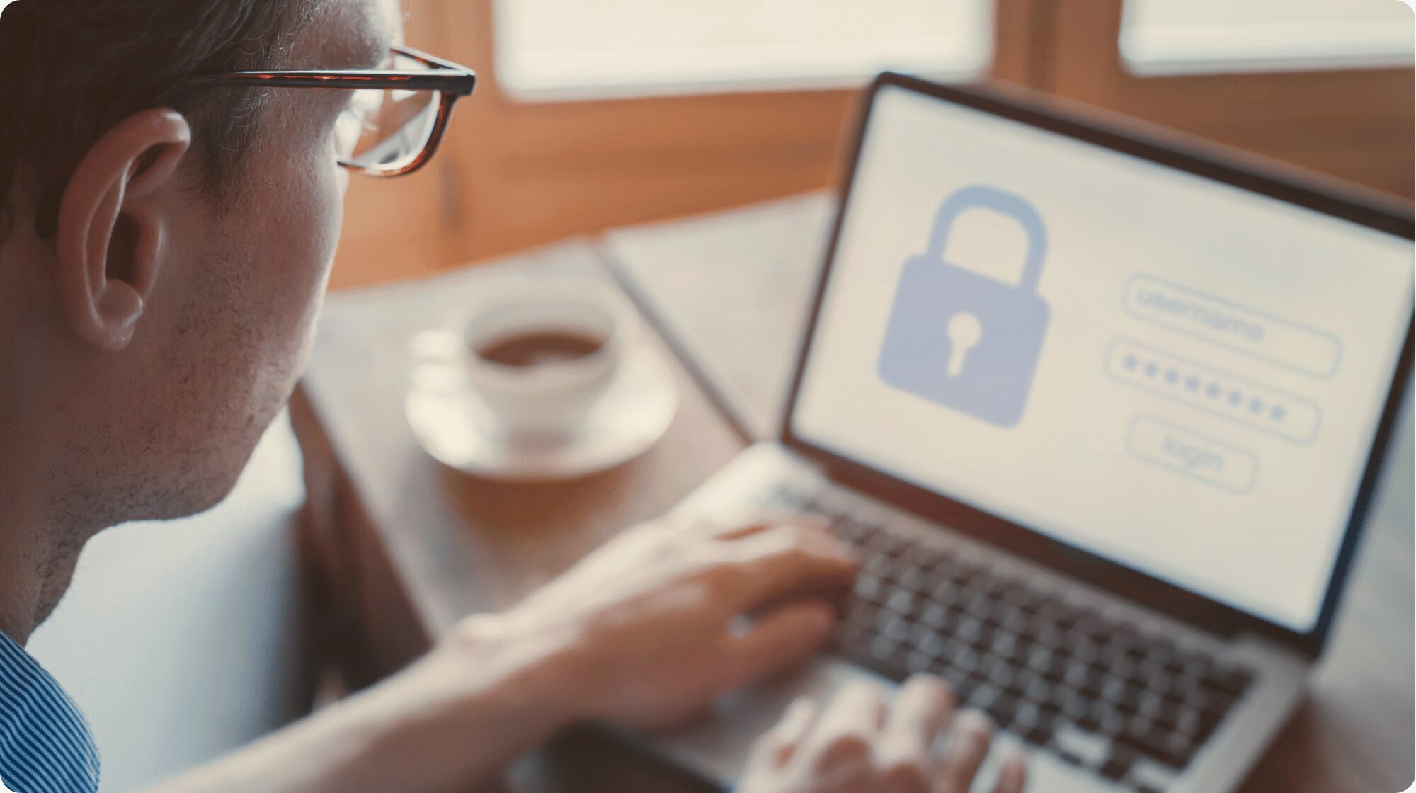 Man with glasses logging into a laptop. The screen shows a blue lock and login screen.