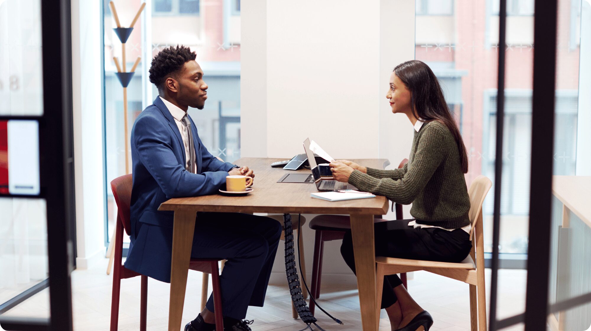 Two people are facing each other across the desk. The lady sitting on the right is interviewing the man on the left.