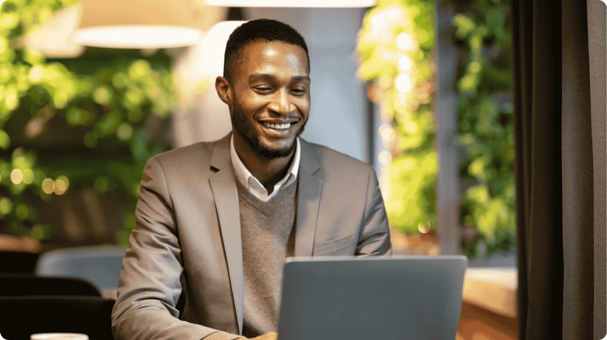 A man is sat at a desk smiling and working on a laptop.