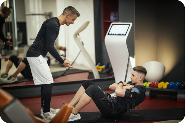 Personal trainer is standing up coaching a young man who is doing sit ups.